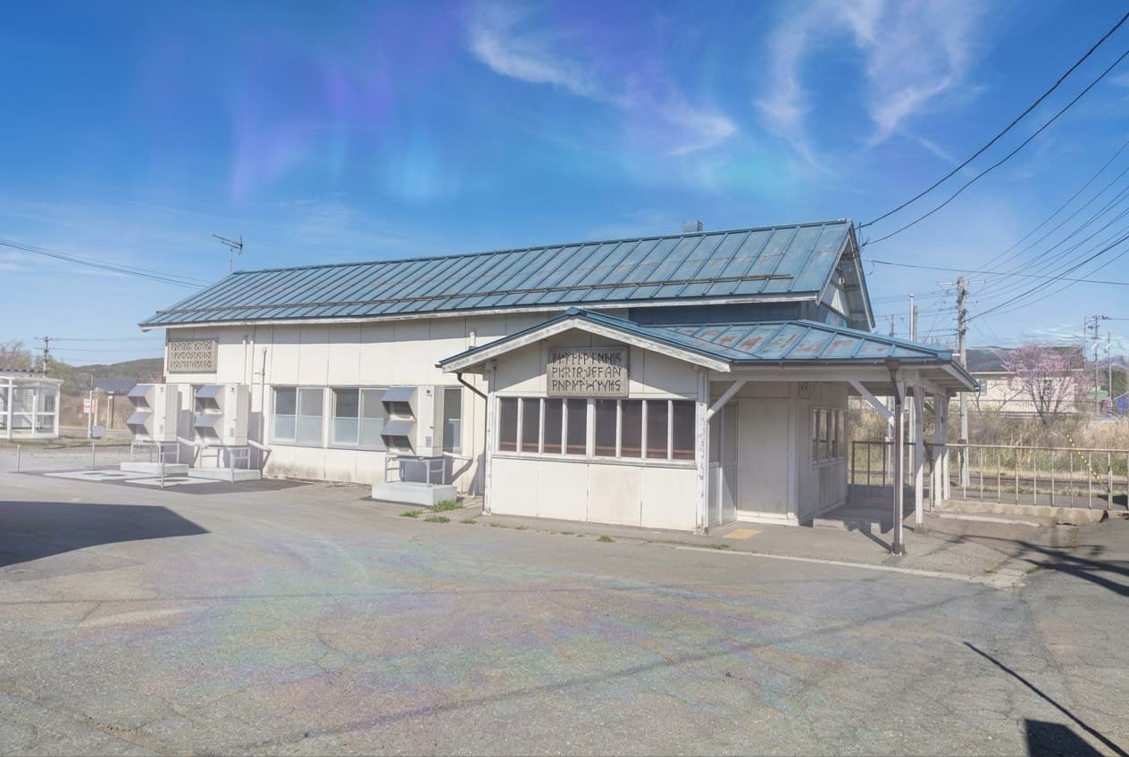 A small railway station building in northern Aomori beneath a bright sky
